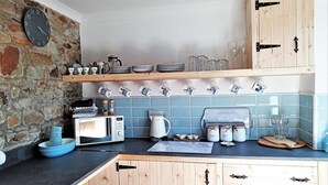 Une cuisine avec un mur en pierre, des armoires en bois, une horloge et divers ustensiles de cuisine.