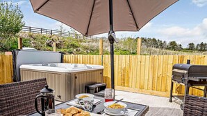 Une terrasse dotée d’un jacuzzi, d’un barbecue, de fauteuils en osier et d’une table préparée pour le petit-déjeuner.