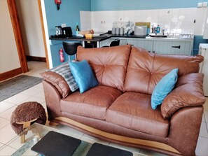 Ein braunes Ledersofa mit blauen Kissen in einem Raum, im Hintergrund ist eine Küche zu sehen.