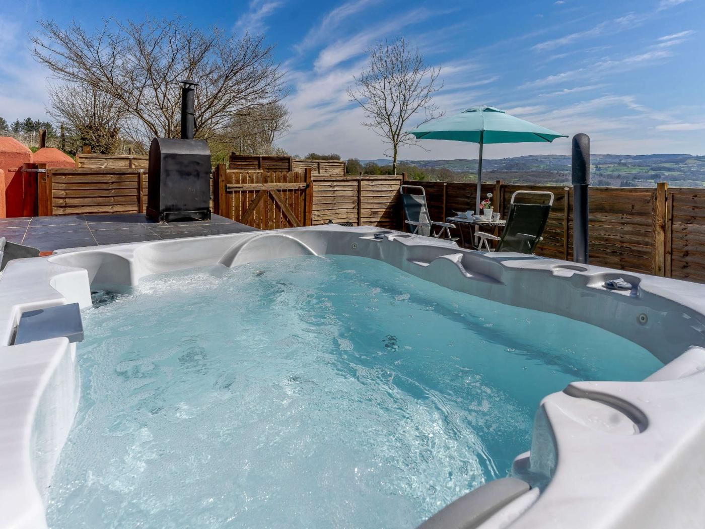 A hot tub with a wooden deck and a view of the countryside.