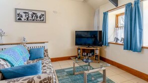 Ein Wohnzimmer mit einer Couch, einem Glastisch, einem Fernseher und einem Fenster mit Vorhängen.
