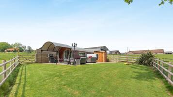 Un bâtiment de style rustique, évoquant une ferme, avec un toit incurvé, un espace barbecue et un petit abri en bois.