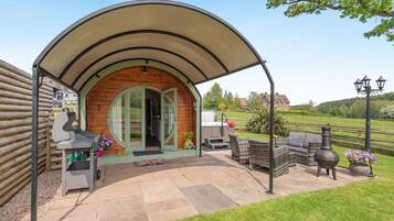 Un espace extérieur abrité, aménagé avec un barbecue, du mobilier de jardin et un drapeau planté dans le sol.