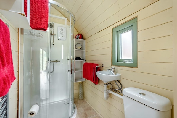 A bathroom with a glass shower enclosure, a white sink, a toilet, and a window with a green frame.