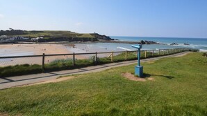 A coastal view with a grassy area, a pathway, and a beach with people. - 1 Bed in Launceston (oc-81332) (Saint Giles on the Heath)