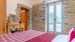 A bedroom with a bed, a wooden dresser, a mirror, and a stone wall. - 1 Bed in Launceston (oc-81332) (Saint Giles on the Heath)