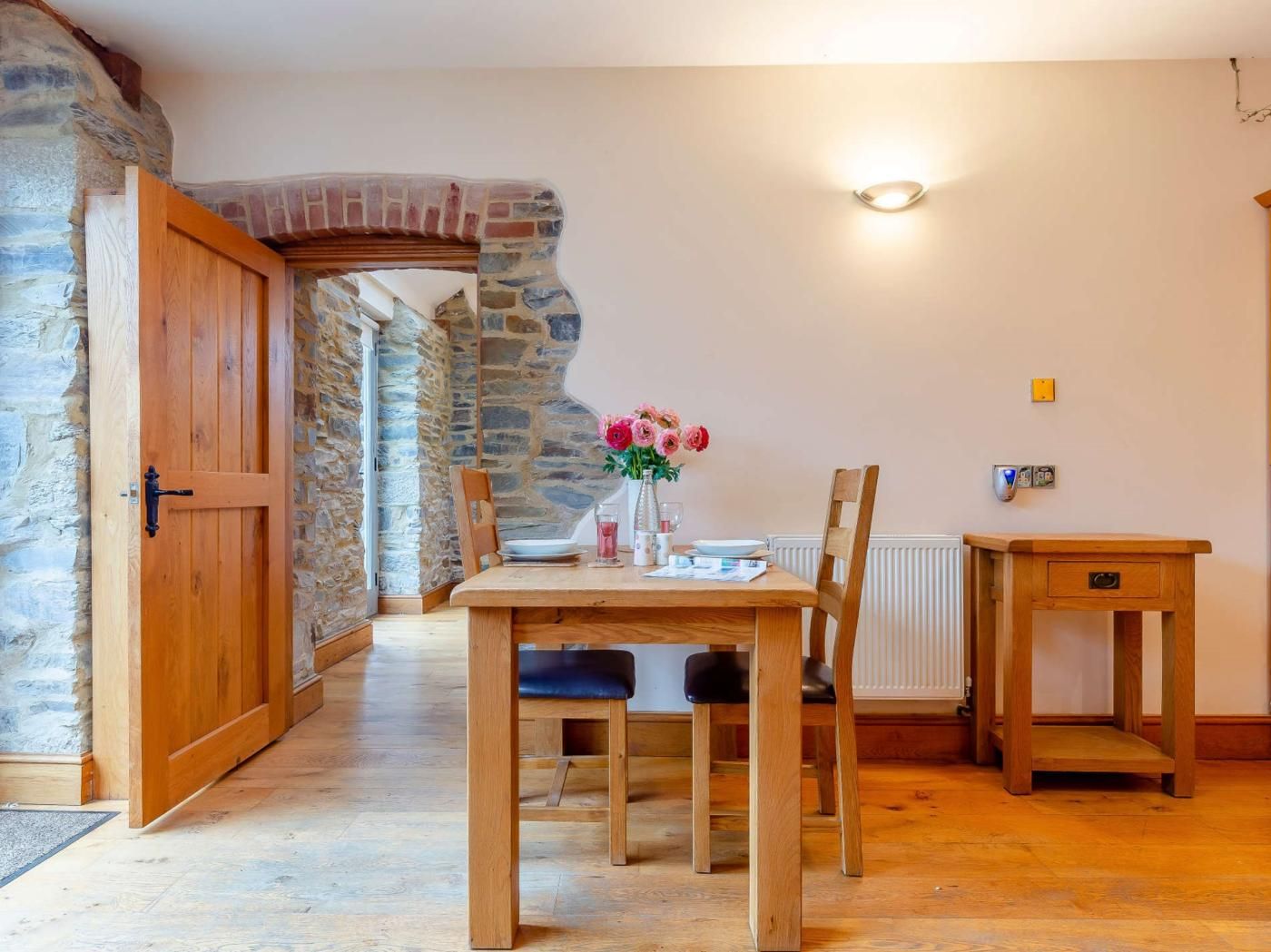 Zona pranzo con parete in pietra, porta in legno e tavolo imbandito per due persone con sedie.