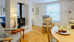 Een gezellige woonkamer met een open haard, een eethoek met een tafel en stoelen, en een bank.