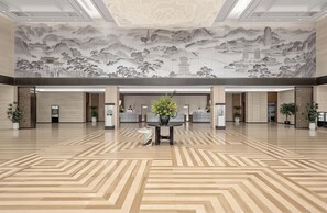 A spacious lobby with a traditional mural, a reception desk, and potted plants.