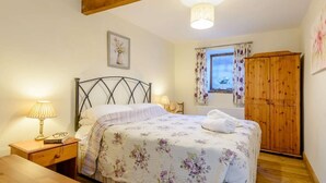 Ein Schlafzimmer mit einem Bett, Nachttisch, Lampe, Kleiderschrank und einem Fenster mit Vorhängen.