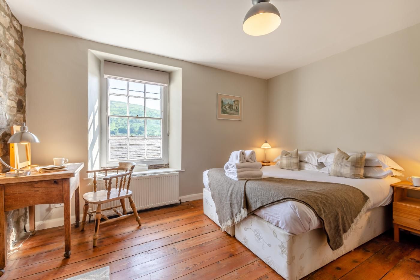 A bedroom with a bed, bedside table, lamp, chair, and a window with a view.