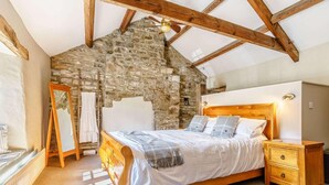A bedroom with a stone wall, wooden beams, a bed with a wooden headboard, a nightstand, and a mirror. - 5 Bed in Richmond (oc-81457) (Gunnerside)