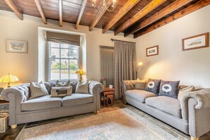 Ein gemütliches Wohnzimmer mit zwei Sofas, einem Tisch und einem Fenster mit Vorhängen.