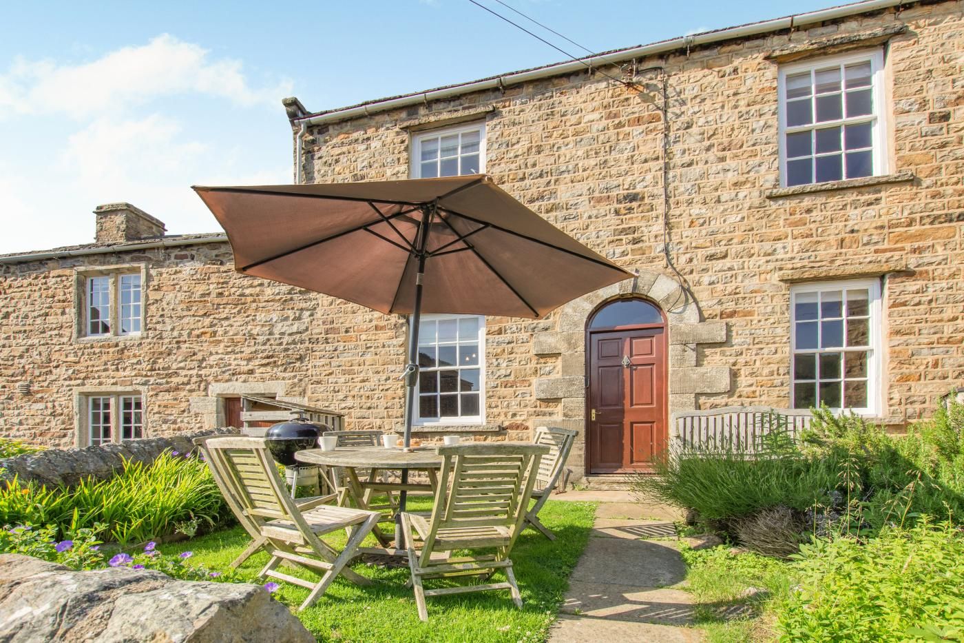 A stone building with a patio area featuring a table, chairs, and a barbecue grill.