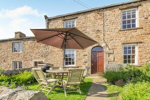 A stone building with a patio area featuring a table, chairs, and a barbecue grill. - 5 Bed in Richmond (oc-81457) (Gunnerside)