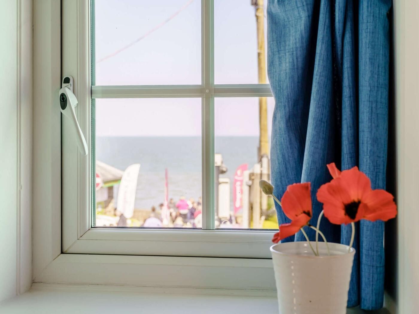 A window with a view of a beach, a white door, and a vase with flowers.