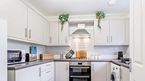 A modern kitchen with white cabinets, a built-in oven, a microwave, a toaster, and a washing machine. - 3 Bed in Cromer (oc-81481) (Overstrand)