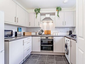 Eine moderne Küche mit weißen Schränken, einem eingebauten Backofen, einer Mikrowelle, einem Toaster und einer Waschmaschine.