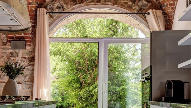 A kitchen with a brick archway, modern cabinetry, and a view of greenery outside. - Casa Carlin, Cascine Crema: large house that sleeps up to 11 people, with a 20x14 m pool (Piemonte)