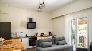 A modern kitchen with a built-in stove, a black range hood, and a coffee maker. There is a grey sofa and a small white table with candles. - Stavros Two-Bedroom House by Konnect (Corfu)