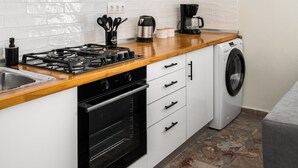 A modern kitchen with a gas stove, oven, microwave, and a built-in washing machine. - Stavros Two-Bedroom House by Konnect (Corfu)