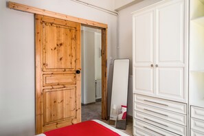 A bedroom with a wooden door, a white wardrobe, and a bed with a red blanket. - Stavros Two-Bedroom House by Konnect (Corfu)