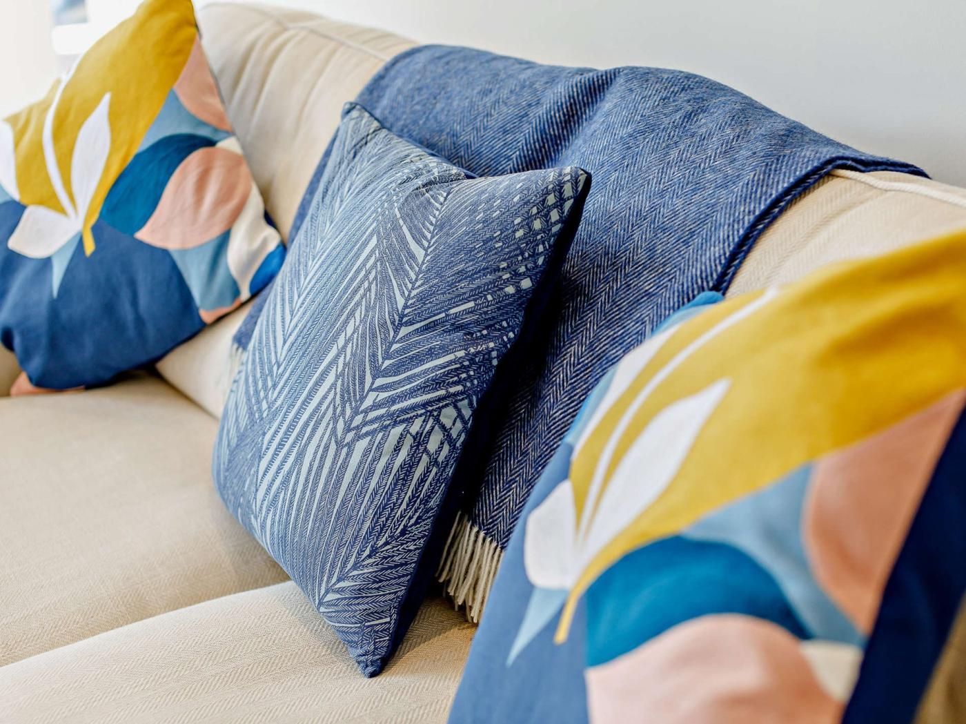 Ein Sofa mit mehreren Kissen, darunter ein blaues gemustertes und ein blumiges in Gelb und Weiß.