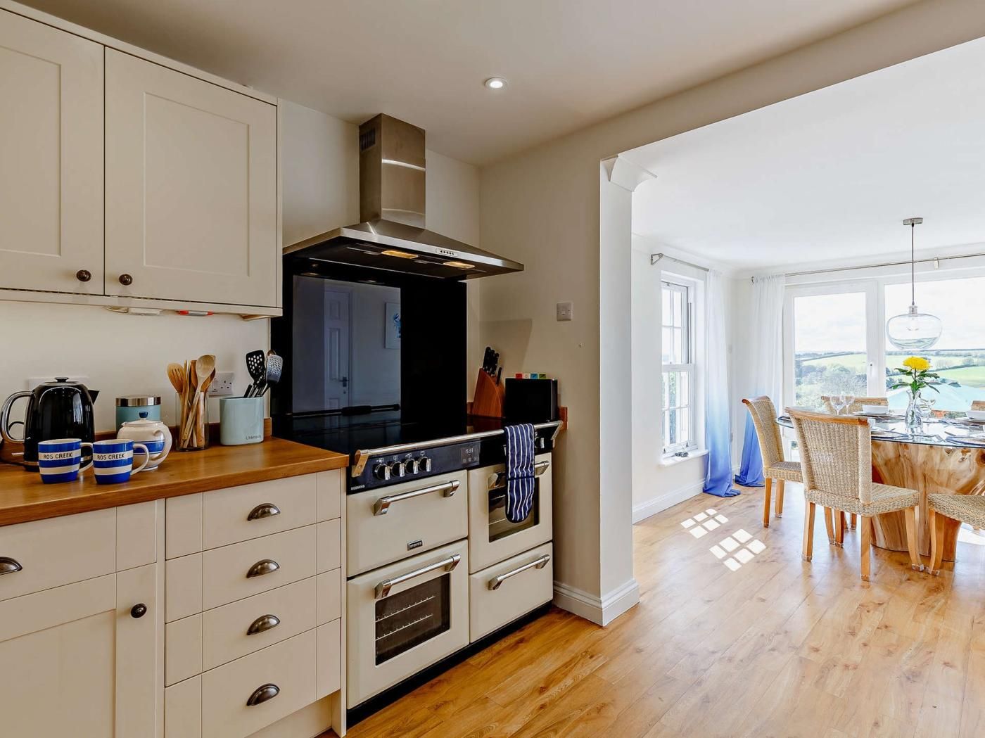 A modern kitchen with white cabinetry, a black stove, and a dining area with a view.