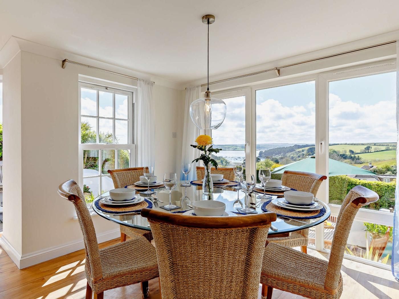 A dining area with a round table, wicker chairs, and a view of a lake.