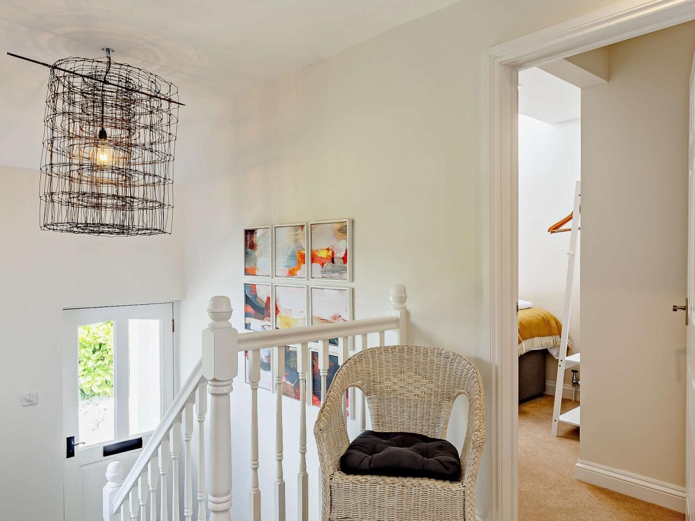 A staircase with white railings, a wicker chair with a cushion, and a wall with abstract art.