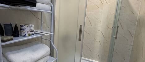Un bagno con doccia nell'angolo, un WC e uno scaffale con asciugamani e articoli da toilette.