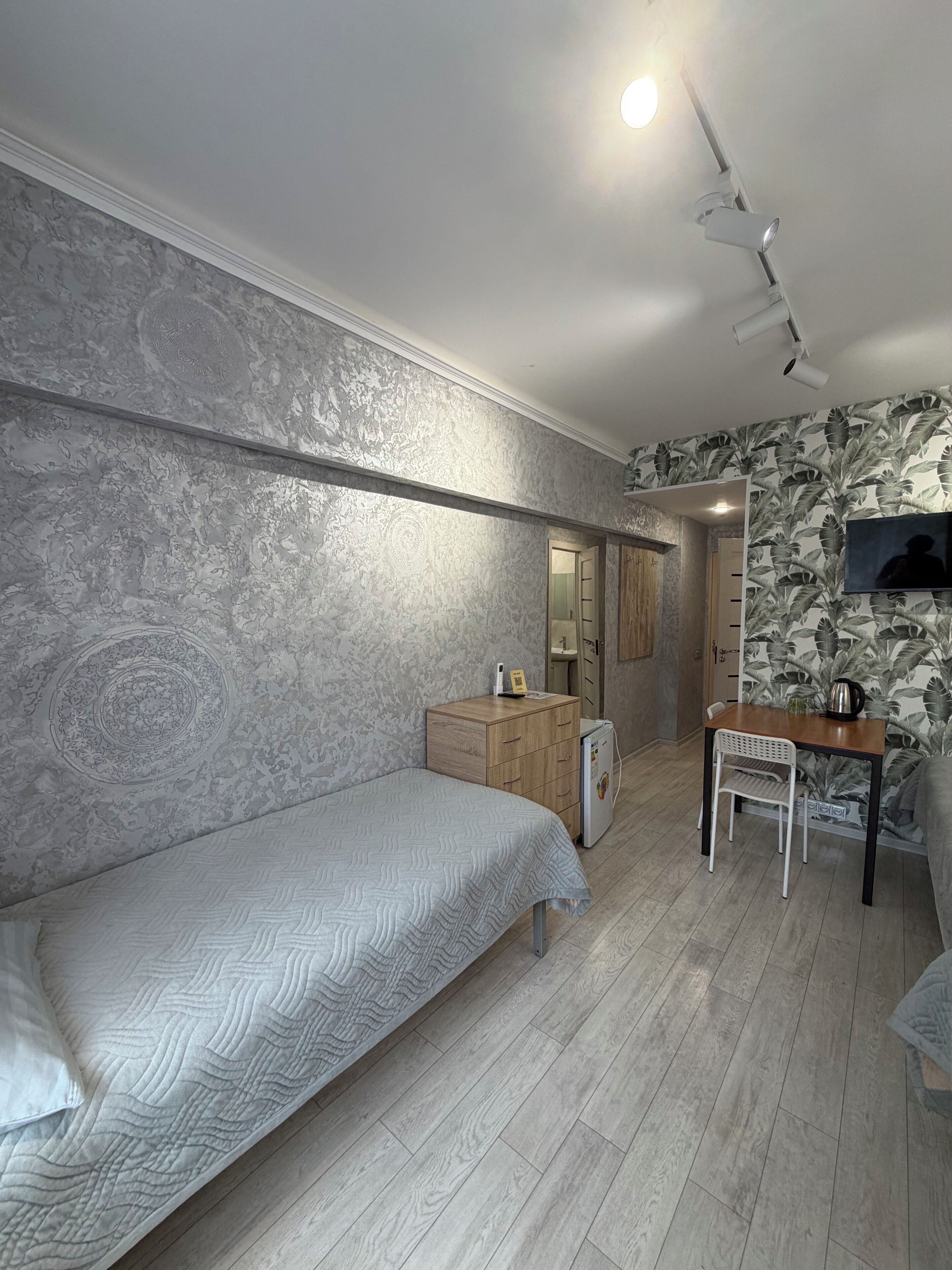 A bedroom with a bed, a desk, a chair, a wardrobe, and a television.