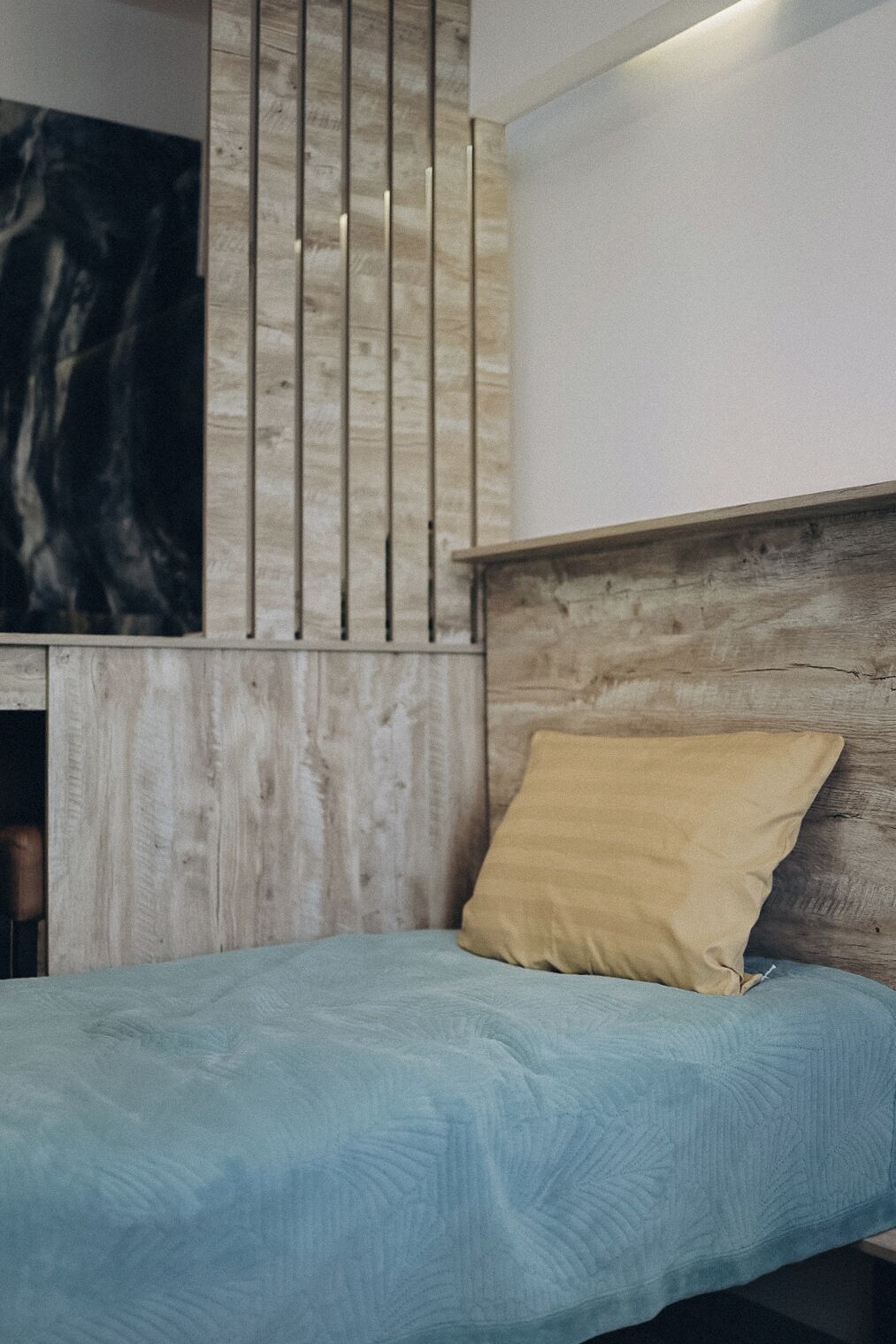 A bedroom with a bed, a wooden headboard, a wall with vertical slats, and a large abstract painting.