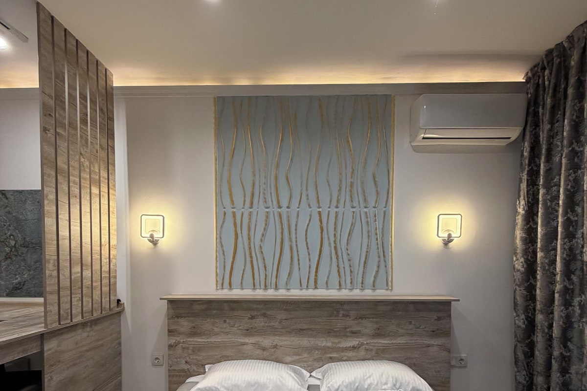 A modern bedroom with a large bed, two wall-mounted lights, and an air conditioning unit.