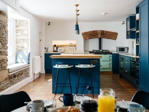 Eine moderne Küche mit einer zentralen Kochinsel, Barhocker, einer Steinwand und Blick ins Freie.