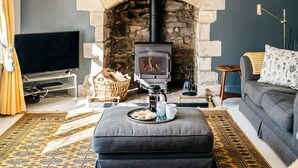 A cozy living room with a stone fireplace, a sofa, a television, and a coffee table. - 8 Bed in Newquay (oc-81510) (Quoit)