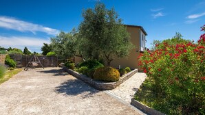 A residential property with a paved driveway, a wooden gate, a stone wall, and a variety of plants including a large tree and flowering bushes. - Casa Aneri by Villas Guide (Pavicini)
