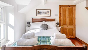 Une chambre à coucher avec un lit en bois, du linge de lit blanc, un tableau encadré au mur et une porte en bois.