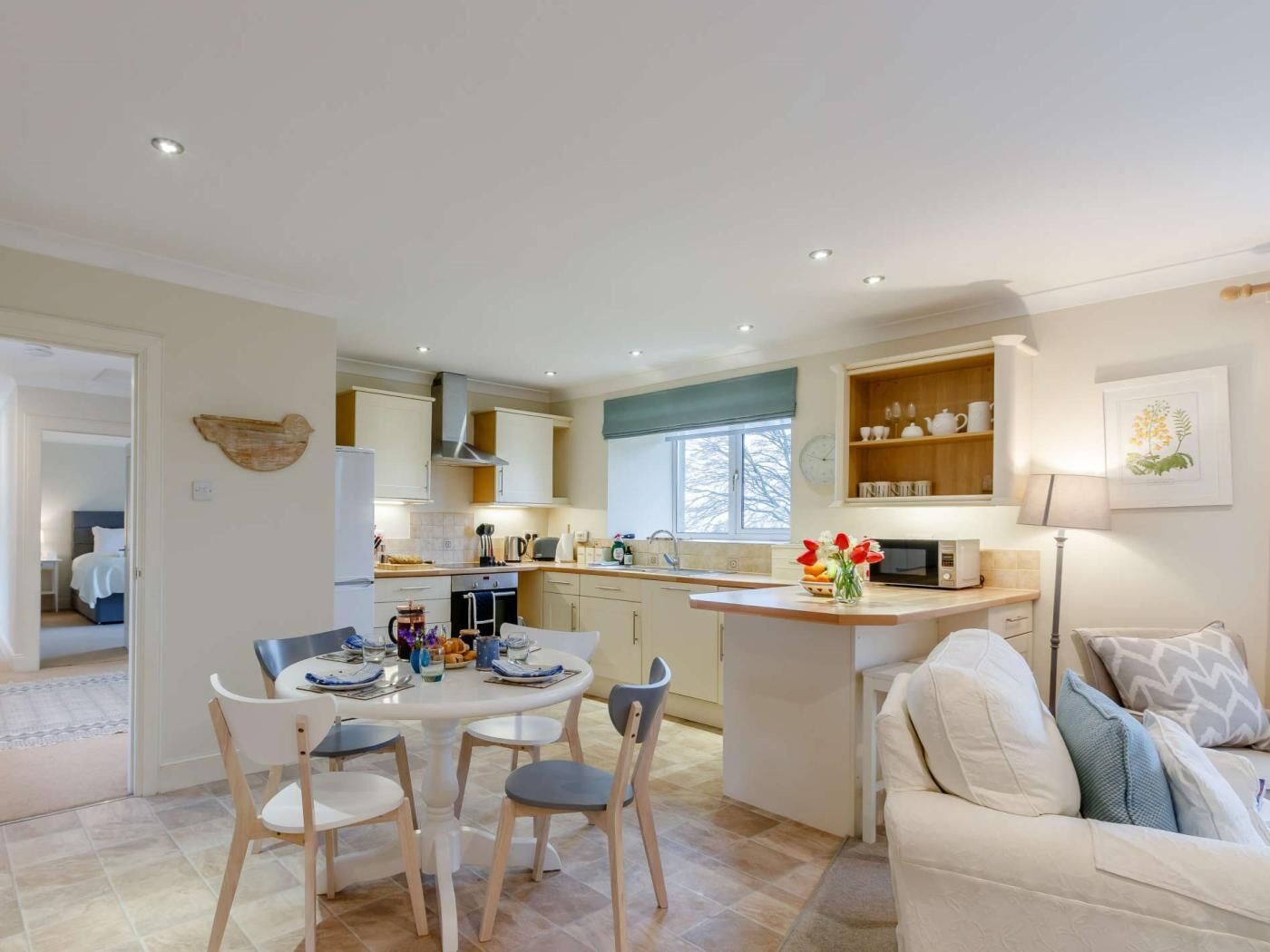 A modern kitchen with a dining area, a sofa, and a small island with a vase of flowers.