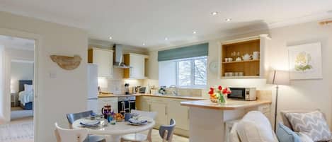 A modern kitchen with a dining area, a sofa, and a small island with a vase of flowers.