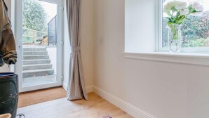 Una habitación con puerta corrediza de vidrio, ventana con vista a follaje y un florero con flores en el alféizar.