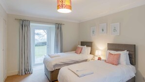 Habitación de hotel con dos camas, un ventanal con cortinas, una lámpara en el techo e imágenes enmarcadas en la pared.