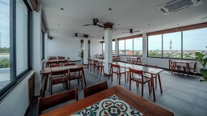 A spacious dining area with multiple tables and chairs, large windows offering a view of the city, and ceiling fans. - Sonitori Riverside (Siem Reap)
