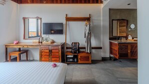 Habitación de hotel con cama, escritorio con televisor de pantalla plana, armario, baño con espejo y zona de ducha.
