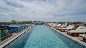 Piscina infinita en la azotea con sillones de descanso y vistas de la ciudad.