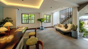 A modern living area with a wooden dining table, chairs, a sofa, and potted plants. - Sonitori Riverside (Siem Reap)