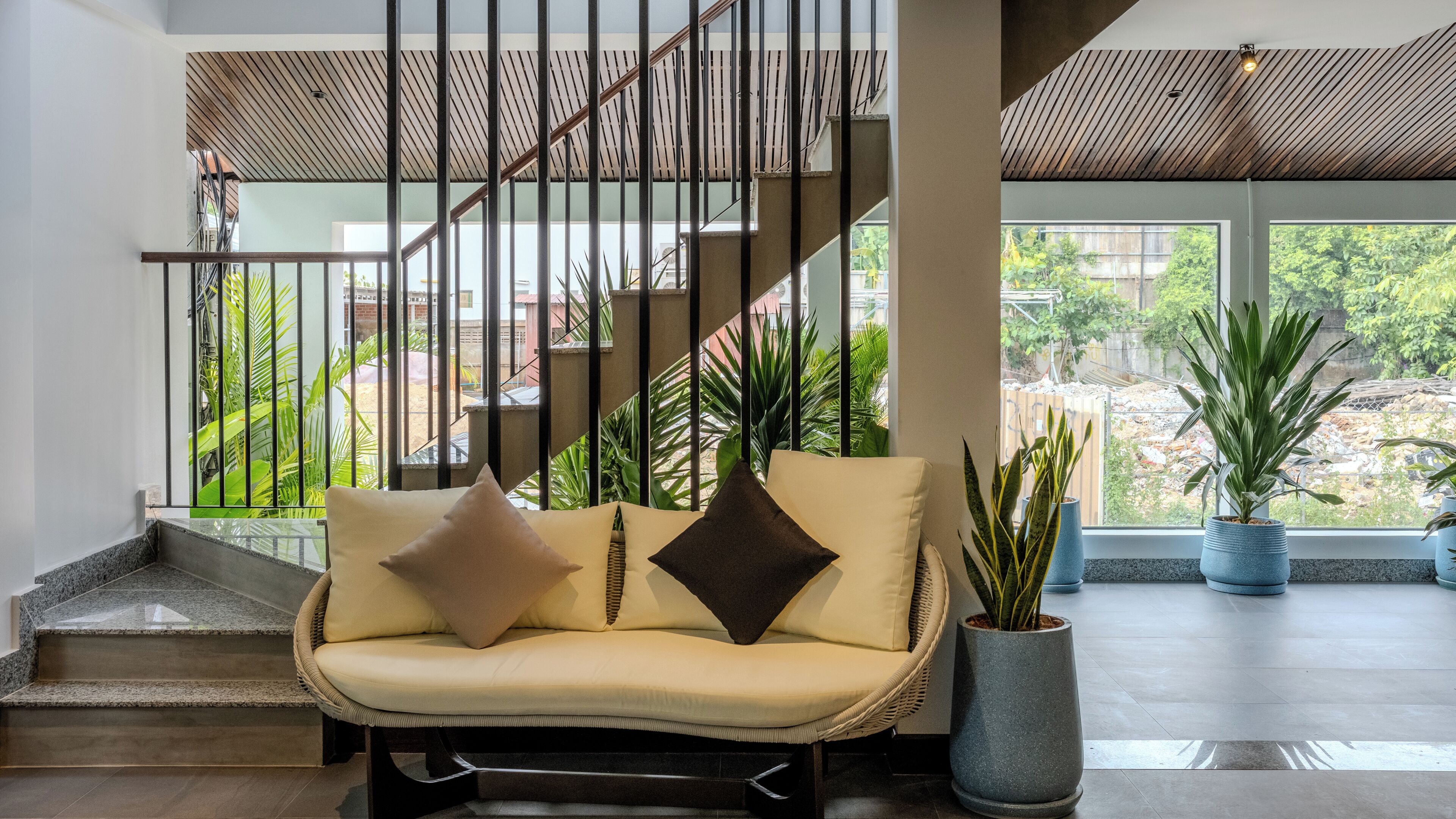 A modern interior with a sofa, staircase, and potted plants.
