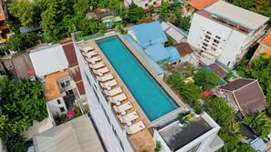 Vista aérea de un hotel con piscina, sillas de descanso y un jardín.