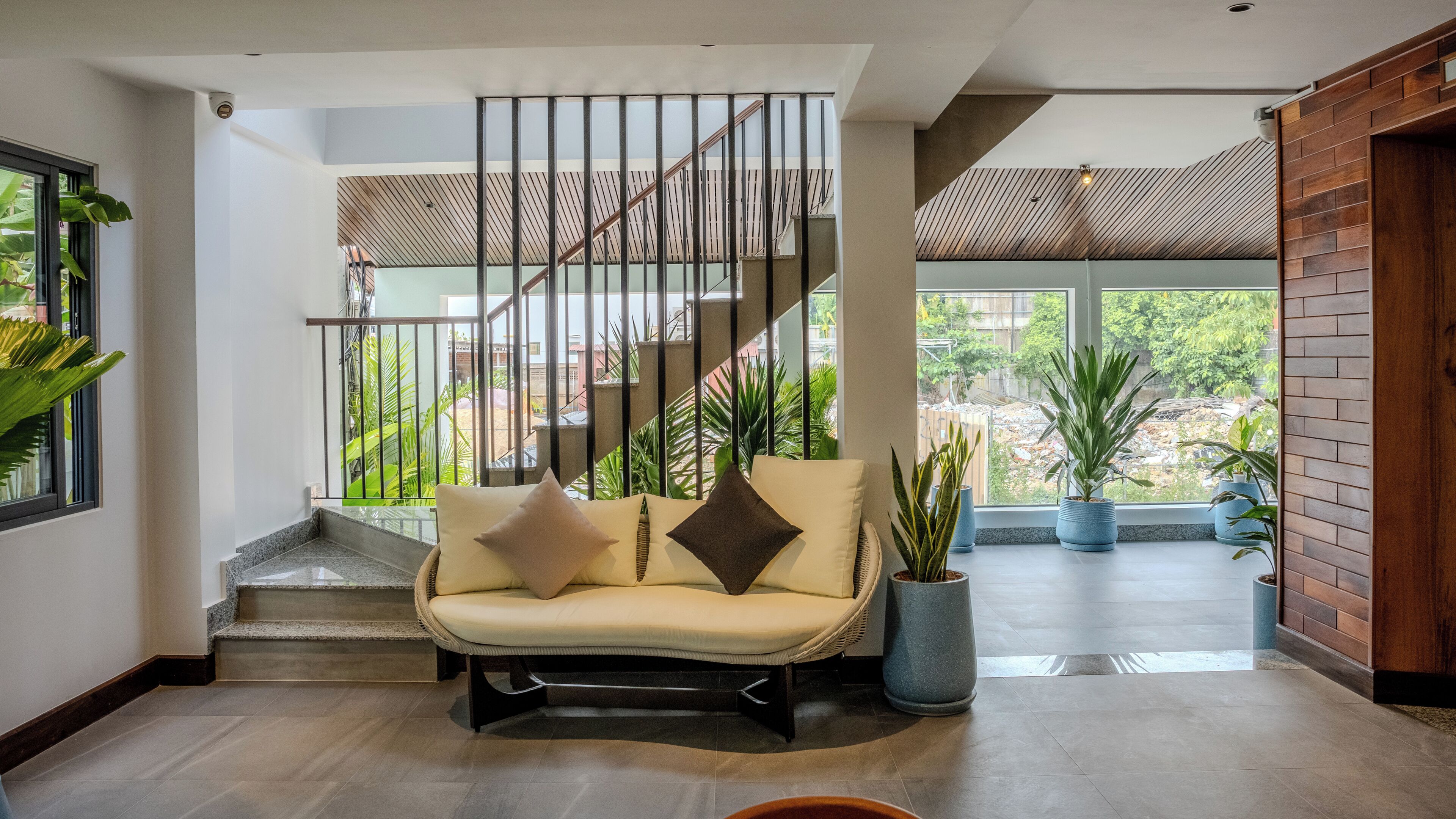 A modern interior with a sofa, staircase, and potted plants.