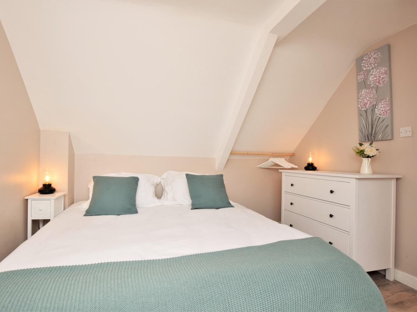 A bedroom with a bed, two pillows, a nightstand, a dresser, and a painting on the wall.
